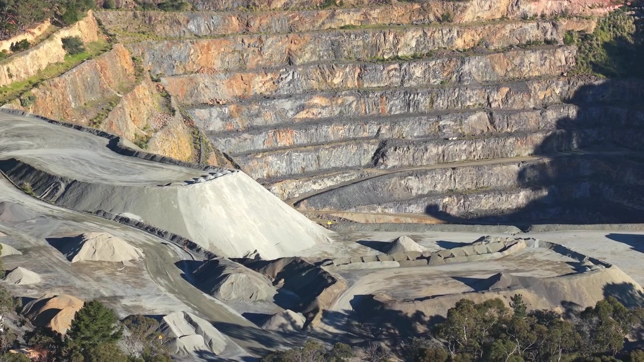 Ampie riprese aeree della cava di Montrose a Melbourne, che mostrano pareti rocciose a gradoni, cumuli di ghiaia e schemi industriali sotto la luce solare intensa. Toni della terra vivaci e un video chiaro da drone dall'alto