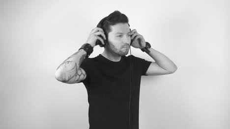 grayscale footage of a tattooed man putting on large studio headphones and beings to dance in slow motion by lifting his arms and fingers up and moving around. man seems happy and enjoying himself.