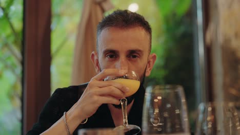 man lifts and sips cocktail in warm restaurant setting with window light
