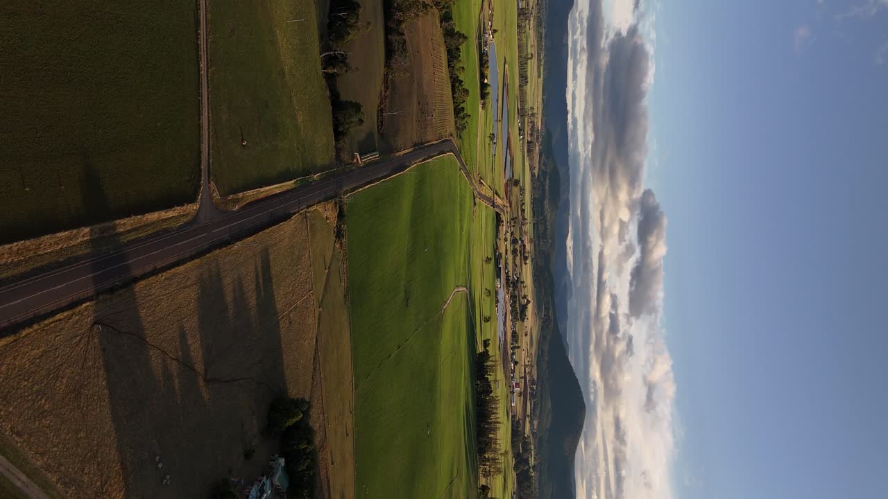 carretera rural que atraviesa campos verdes, interior de tasmania al atardecer, australia