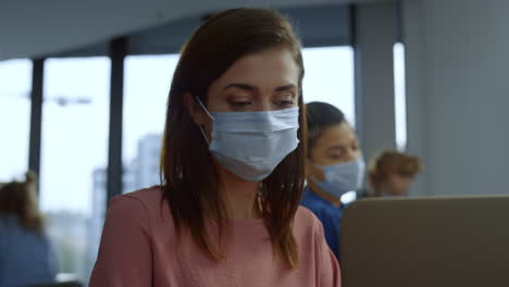 focused businesswoman in medical mask on face working on laptop in office