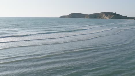 Movimiento-Lento-De-Olas-En-La-Superficie-Del-Mar-Con-Colinas-Y-Costa-Rocosa-En-La-Distancia