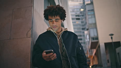 zoomer texting mobile phone lit by city night ambiance closeup. hispanic guy