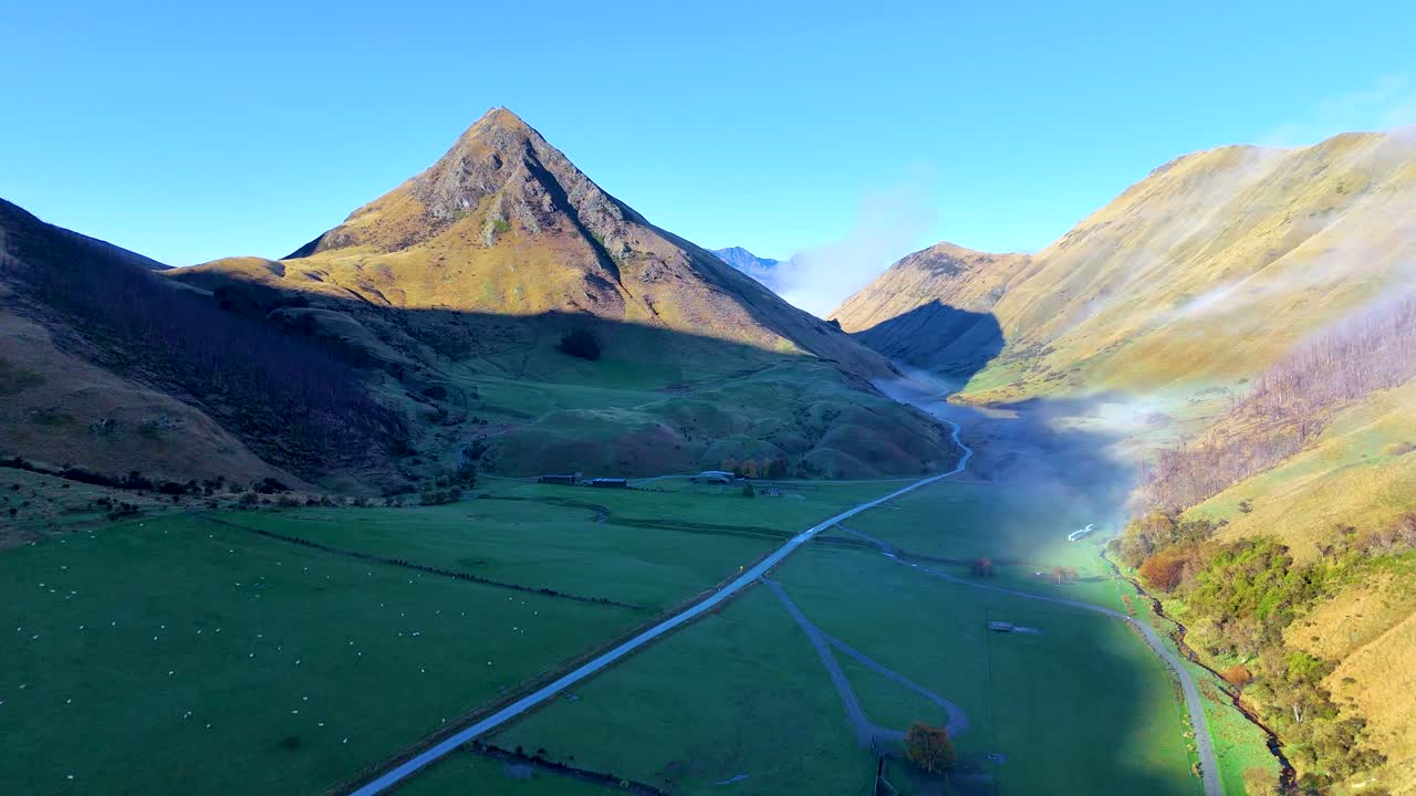 Aerial footage captures the serene landscape of Moke Lake, Queenstown, with misty valleys and sunlit mountains under clear skies
