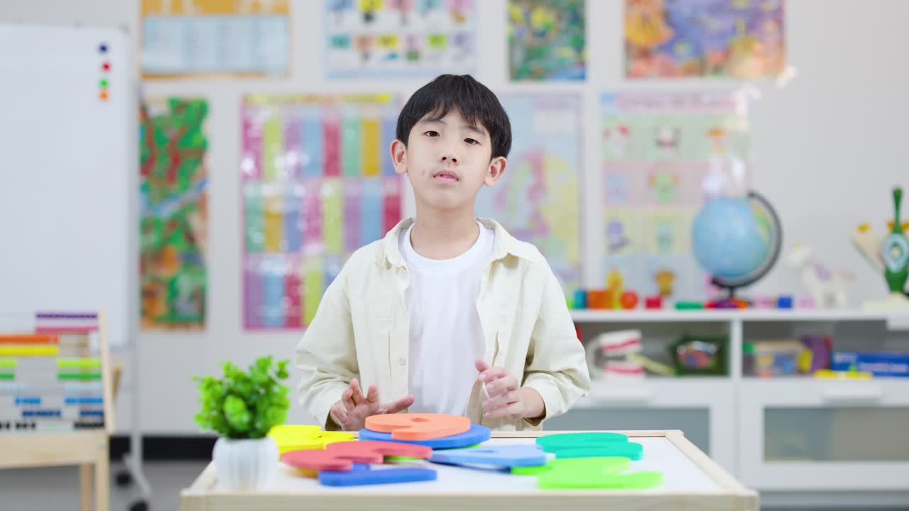 Happy elementary student holds bright foam number six in colorful classroom, static front camera shot