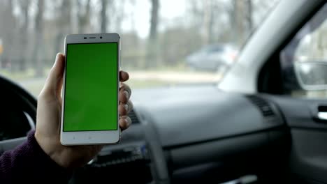 una mano sosteniendo un teléfono inteligente con pantalla verde en blanco en el coche para la dirección, masaje, ubicación, negocio. hombre se sienta en un coche moderno y trabaja en teléfono inteligente - pantalla verde - primer plano. llave de croma.