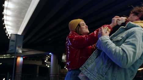 Cheerful-couple-having-fun-outdoor.-Man-and-woman-fooling-with-burgers-in-city.