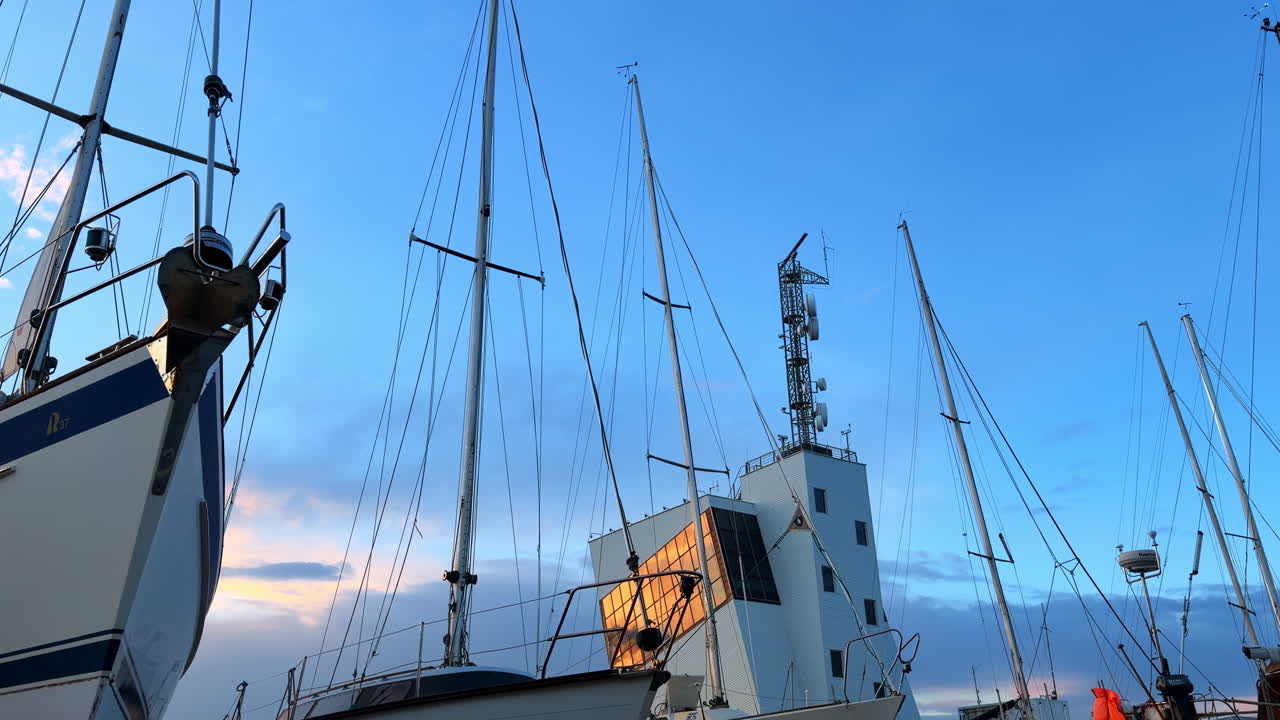 Burgas, Bulgaria, 29 de octubre de 2025: Barcos y una torre se alzan imponentes contra un cielo azul al atardecer cerca del puerto. Los barcos se congregan en el puerto mientras la luz del atardecer se refleja en una torre, creando una vista de mástiles y cielo.