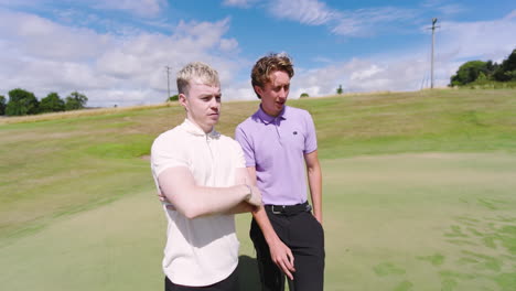male golf players wearing white and blue shirts, holding club and talking on golf course