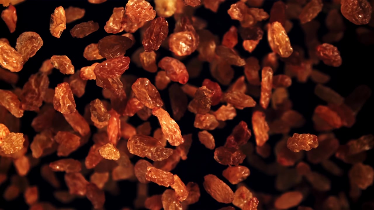 Raisins secs dorés tombant au ralenti sur un fond sombre.