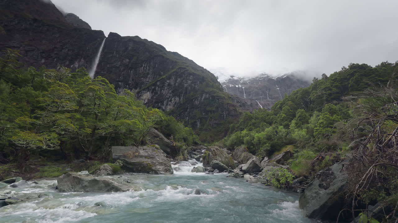 Rapide di un fiume glaciale in una lussureggiante valle verde in Nuova Zelanda con cascate sullo sfondo