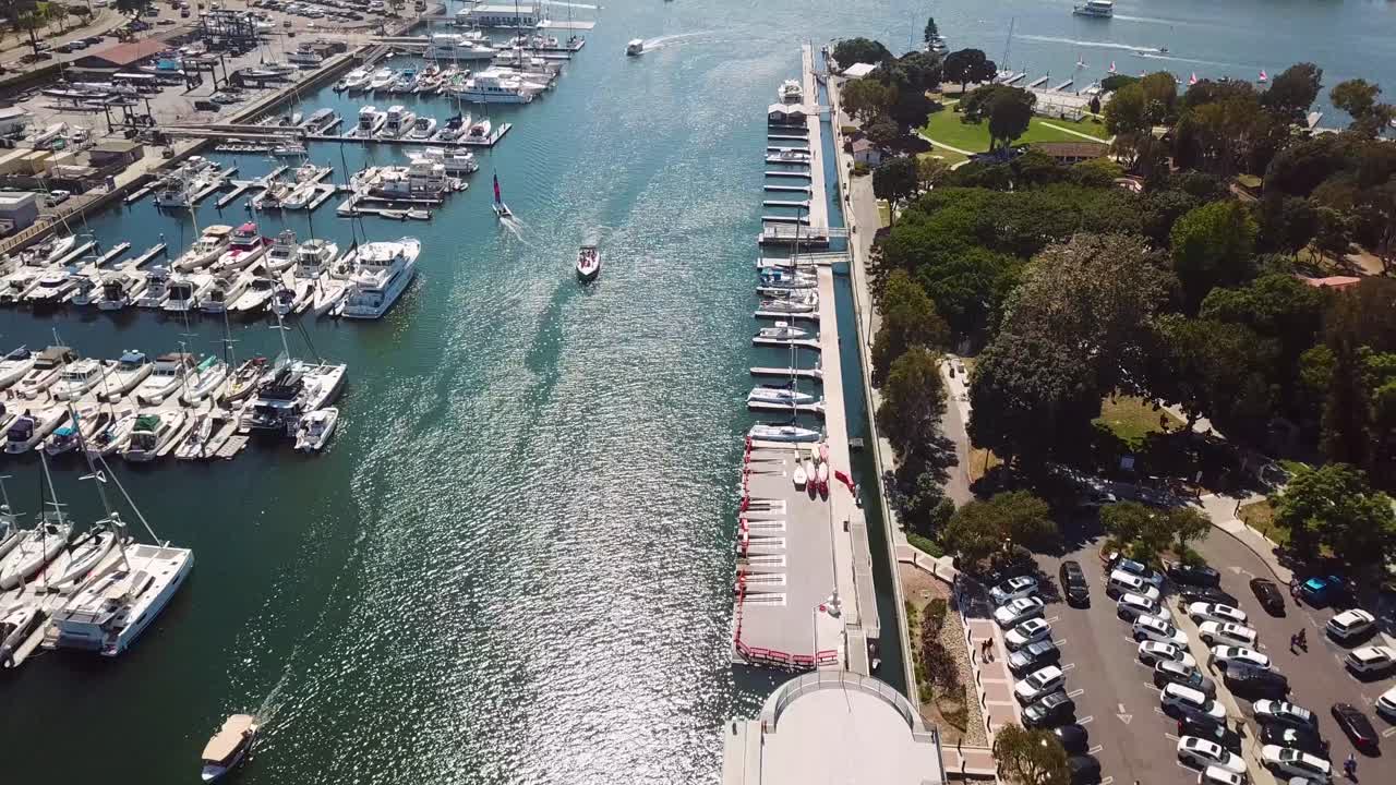 Bird’s eye aerial of Marina del Rey, Los Angeles. The camera tracks laterally from a top down angle across boat slips, docks, and a narrow channel with small craft and sailboats leaving wakes