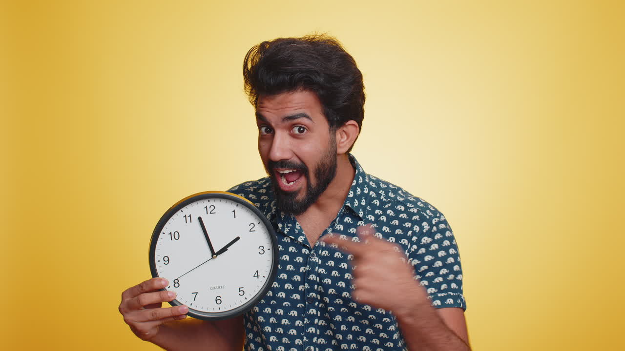 Indian man showing time on wall office clock ok thumb up approve pointing finger at camera