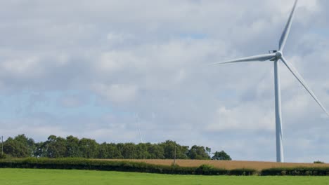 a single wind turbine spins steadily in a green field near edinburgh, scotland, under partly cloudy daylight. static wide shot with natural lighting