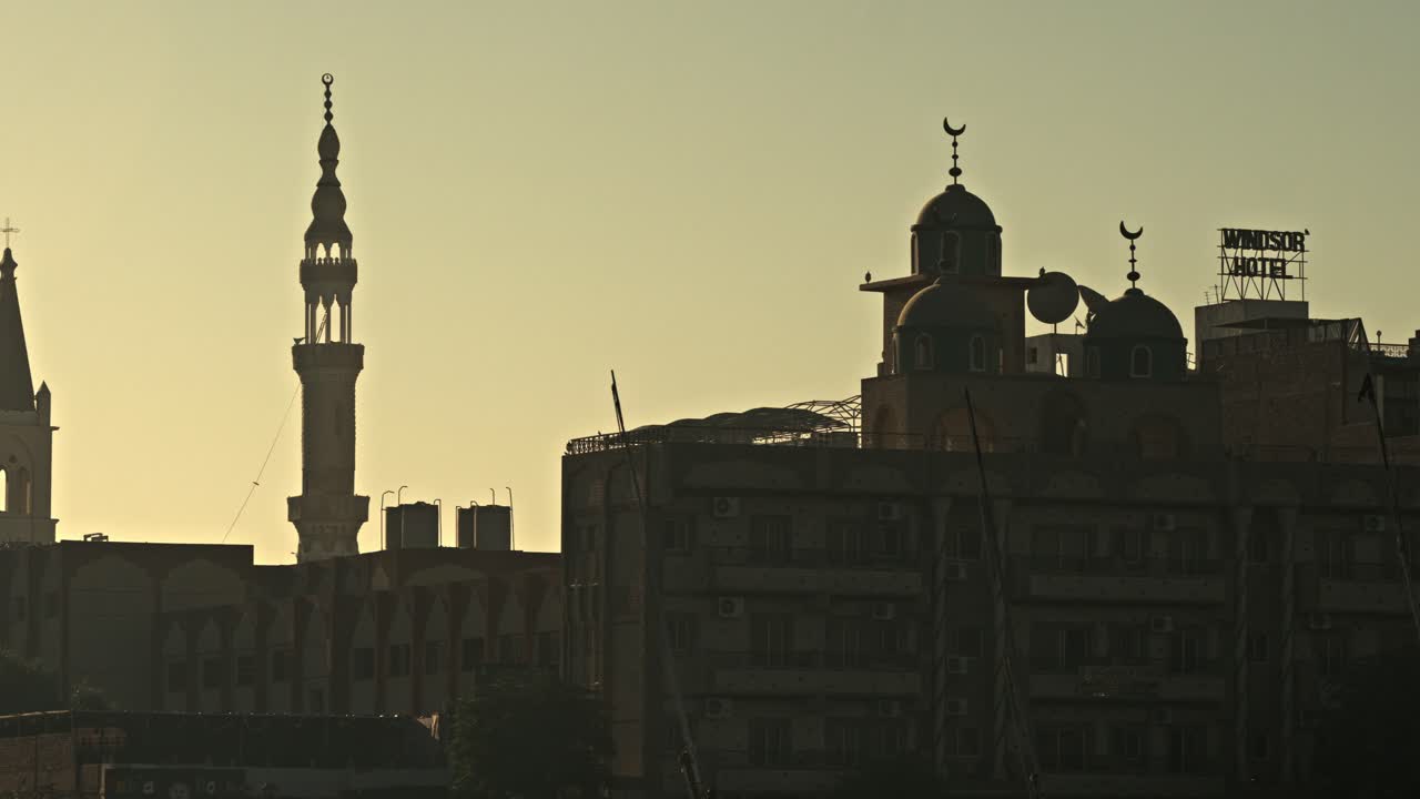 Located along the East Bank of the Nile in Luxor, Egypt, this sunset silhouette features the dual belfries of St. Mary's Coptic Orthodox Cathedral and Sheikh Hammami Mosque