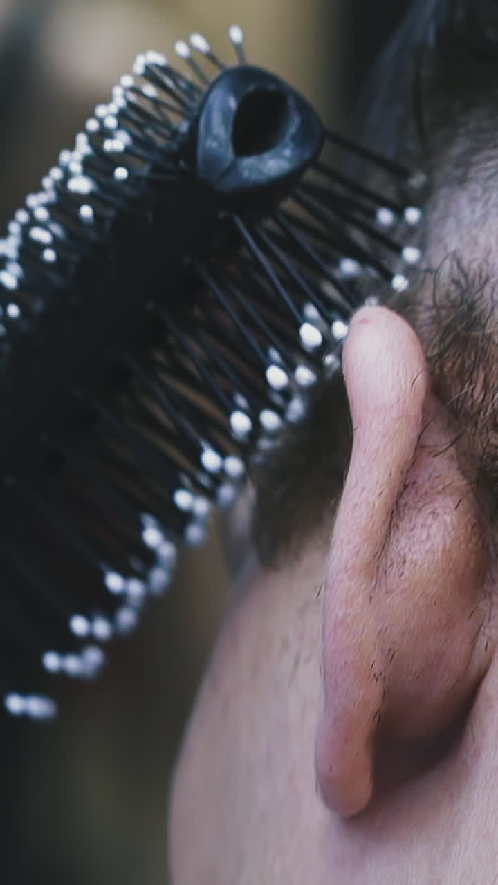 CU, slow motion: male hairstylist does modern haircut to client brushing black hair on temples in modern brightly lit barbershop extreme close view