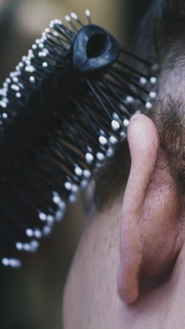 cu, slow motion: male hairstylist does modern haircut to client brushing black hair on temples in modern brightly lit barbershop extreme close view