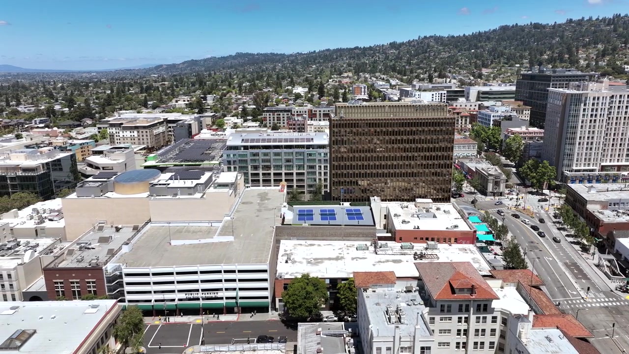 Movimento cinematografico del drone verso sinistra su Berkeley, California, con torri del centro, condomini, quartieri urbani alberati e una catena montuosa panoramica sullo sfondo in una giornata luminosa