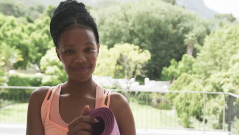 Young-African-American-woman-holds-a-yoga-mat-outdoors,-with-copy-space