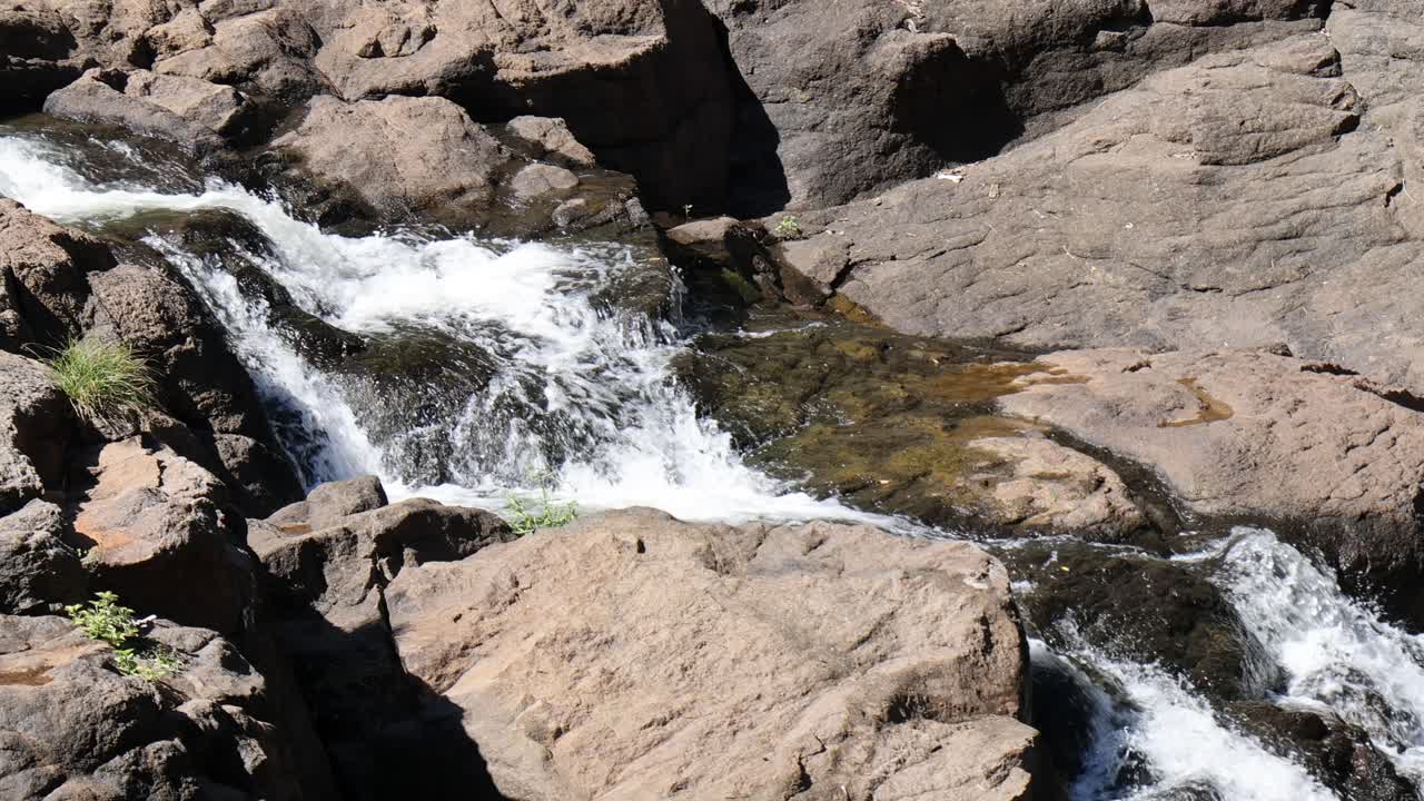 El agua fluye dinámicamente sobre rocas escarpadas bajo la luz del sol