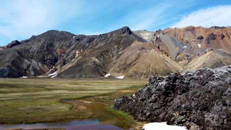 black magma rocks reveal a green valley with patches of snow and colorful rainbow mountains of landmannalaugar in iceland