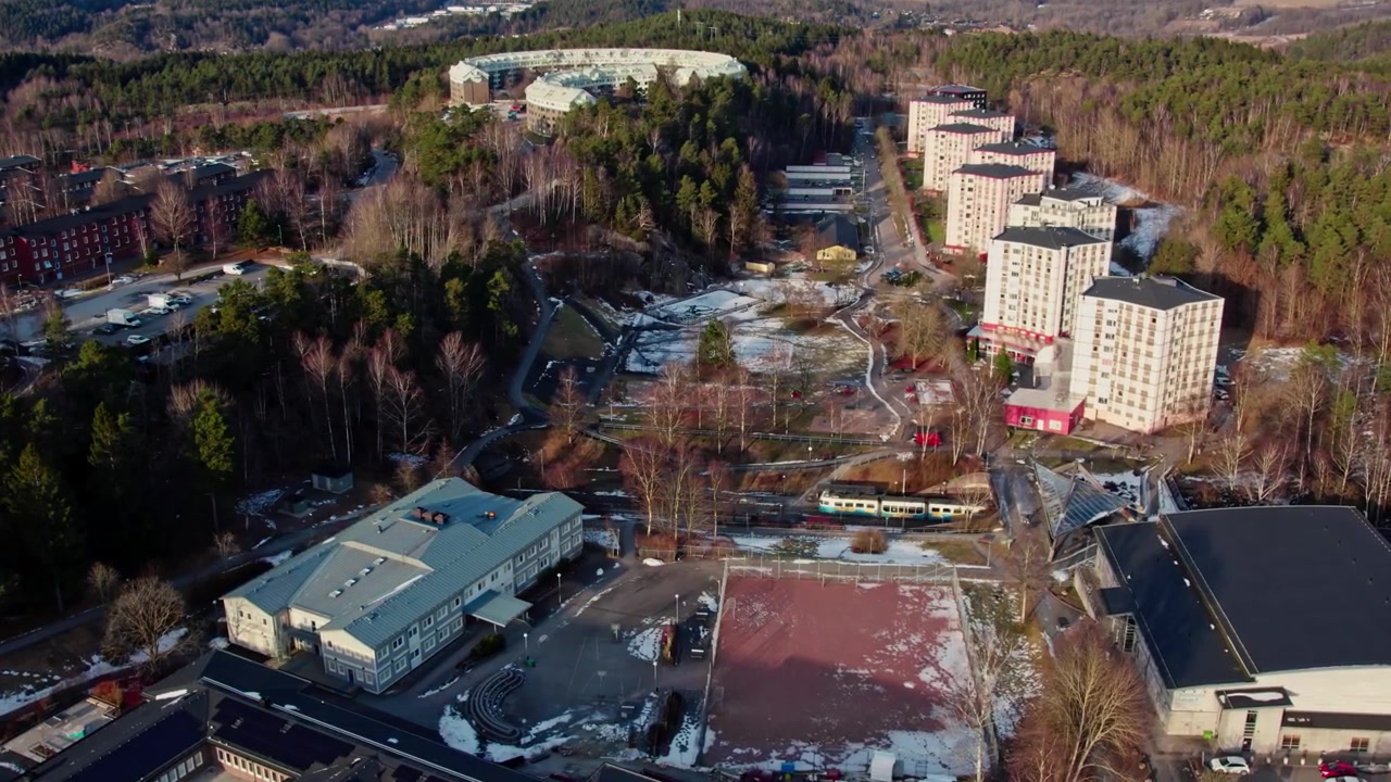 Flygfoto med drönare över bostadshus, vägar, skog och vinterlandskap i ett stadsområde under den kalla årstiden vid Teleskopgatan, Bergsjön, Göteborg, Sverige.