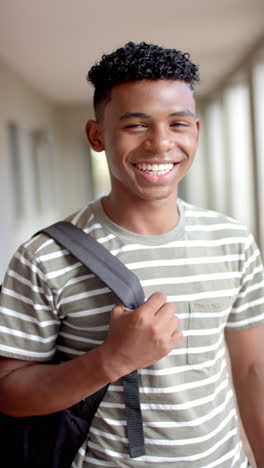 vertical video: in highschool, biracial male teenager with a bright smile holding a backpack strap