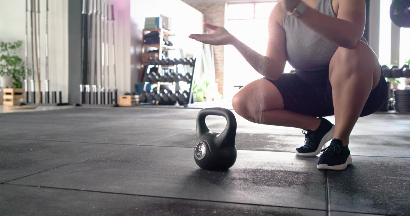 Le gambe di un'atleta stanno entrando nell'area della palestra, si sta cospargendo le mani di magnesite e sta facendo oscillare una kettlebell per la potenza.
