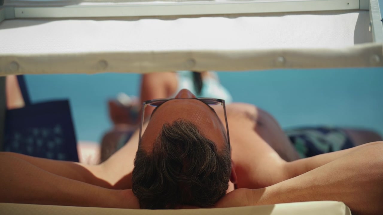 Man relaxing on sun lounger wearing sunglasses near the sea