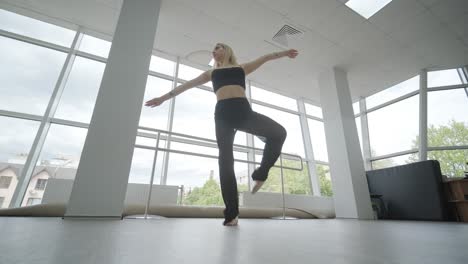 chica en forma con ropa negra actuando contemporáneamente. bailarina muestra movimientos fluidos, cuerpo y manos ondas en la habitación blanca. coreografía de danza de ballet moderno. joven se mueve suavemente