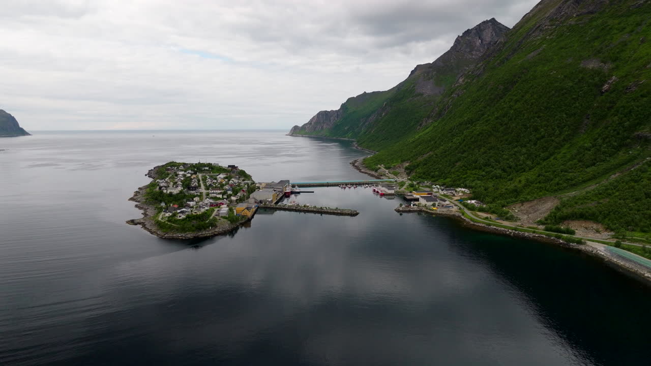 Husøy fishing village on island in Øyfjorden, harbor, bridge, and majestic mountains, Senja, Norway. Aerial backward, copy space