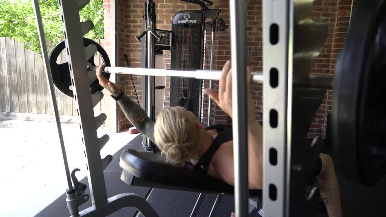 홈 체육관 인클라인 바벨 벤치 프레스에서 문신을 한 남자