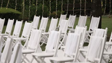 white chairs arranged in rows outdoors for a wedding ceremony, decorated with delicate fabric