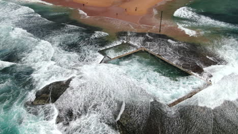 Amplia-Toma-Aérea-De-Olas-Y-Un-Poderoso-Oleaje-Oceánico-Rompiendo-Sobre-La-Piscina-De-Rocas-De-Monavale-En-Un-Turbulento-Día-De-Primavera