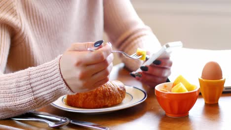 Woman using mobile phone while having breakfast