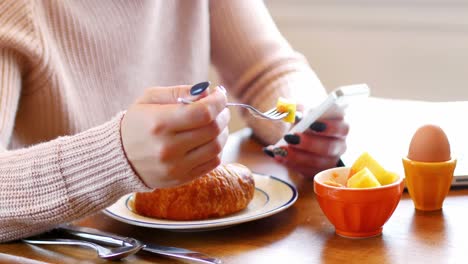 mujer usando teléfono móvil mientras desayuna