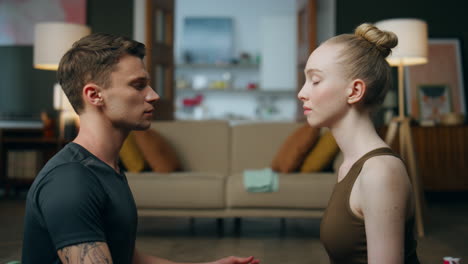 Young-pair-meditating-sitting-opposite-each-other-in-lotus-pose-at-home-closeup.