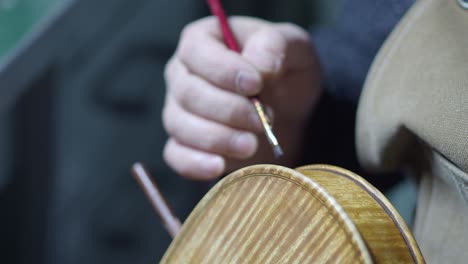 Skilled violinmaker applies antiquing to the marbled ribs and purfling of a violin, revealing the flamed maple pattern on the back plate in workshop setting, captured in close-up detail shot