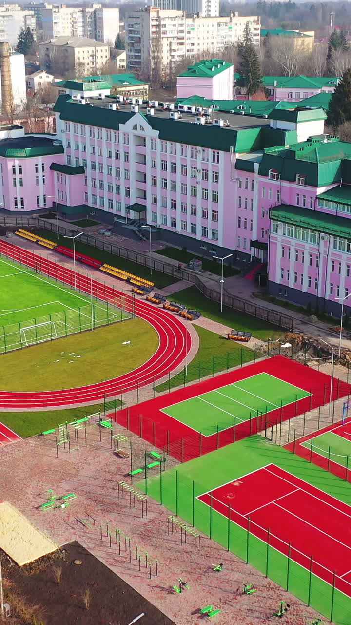 Green and red stadiums near the modern building. Modern outdoor fields for sports in the city. New basketball and football fields. Aerial view. Vertical video