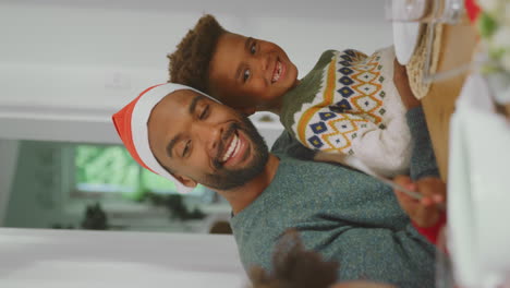Vertikales-Video-Eines-Vaters-Mit-Weihnachtsmütze-Und-Kindern,-Die-Gemeinsam-Zu-Hause-Das-Weihnachtsessen-Genießen