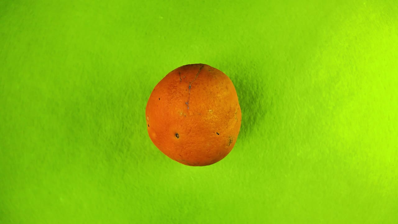 Orange turning gently on green backdrop for fresh, healthy product display or mockup use, top down