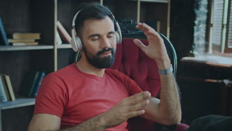 young bearded man sitting in chair listening to music in headphones