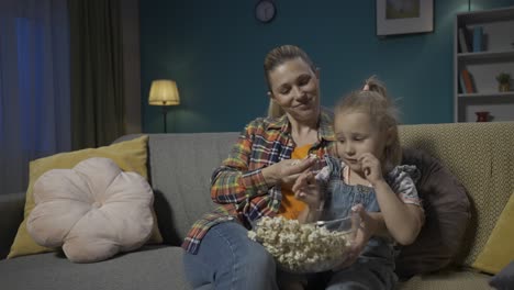 mother and daughter enjoying movie night with popcorn