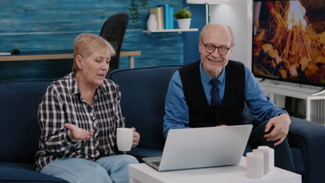 enthusiastic couple of pensioners sitting together on sofa talking on video call
