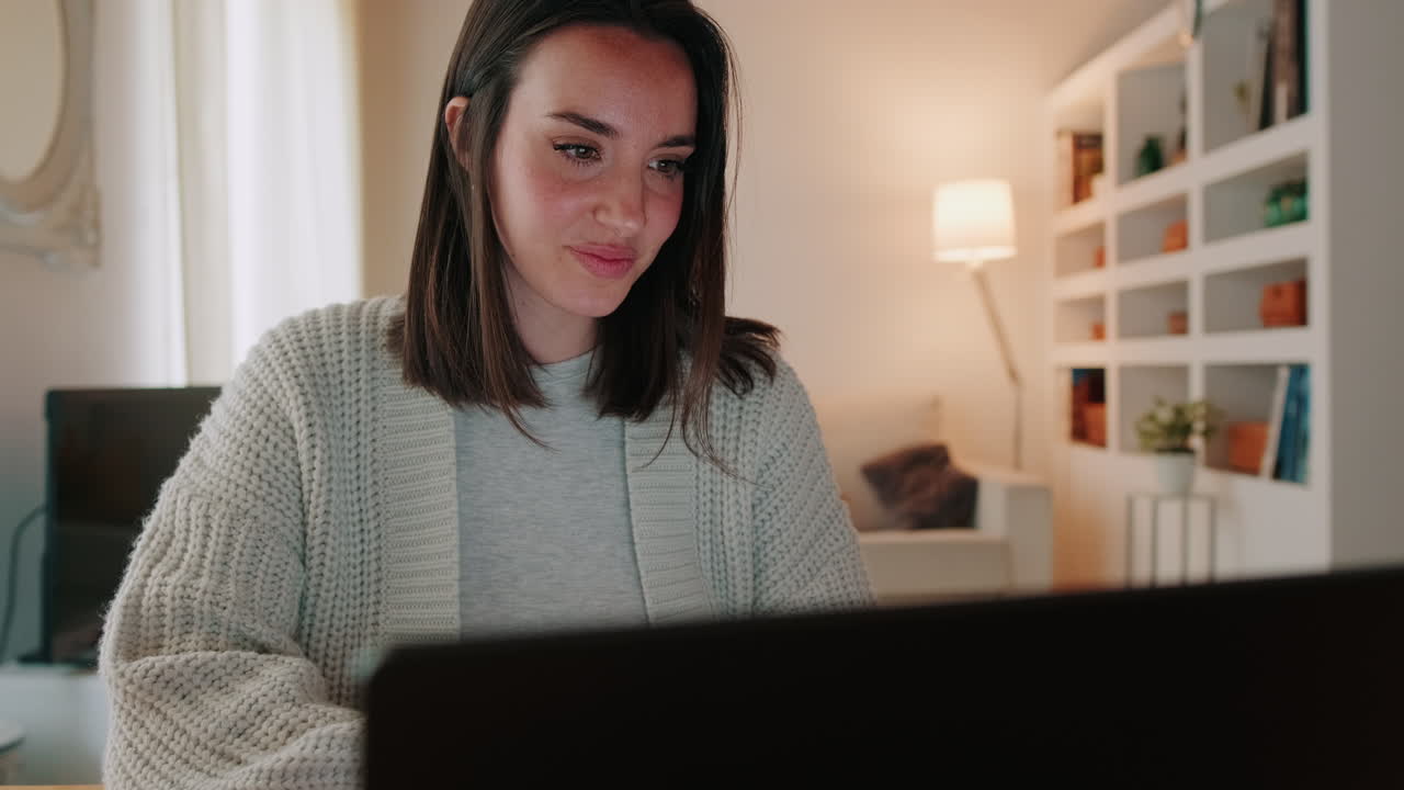 Smilende ung kvinde arbejder på bærbar computer i sit hyggelige hjem