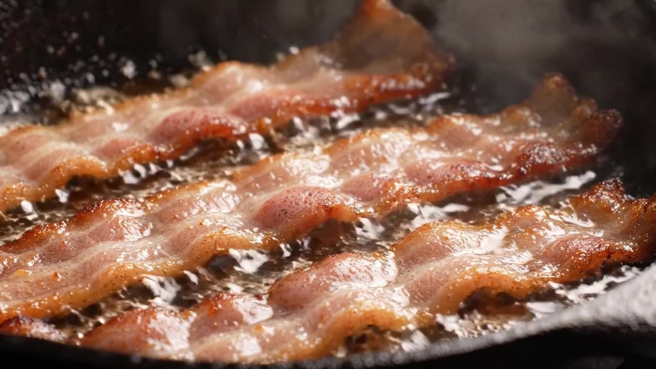 Pancetta sfrigolante che cuoce in una padella calda: strisce croccanti e dorate che friggono alla perfezione in una delizia gustosa e unta.