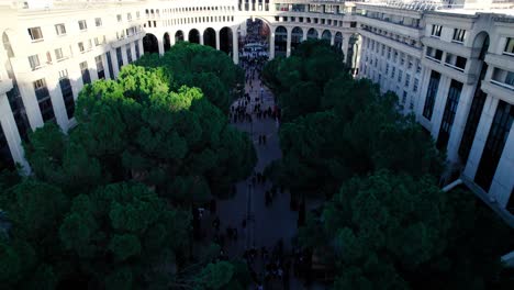 beautiful tilting drone shot of green lush area in the city of montpellier in france with people walking in a square and birds flying by