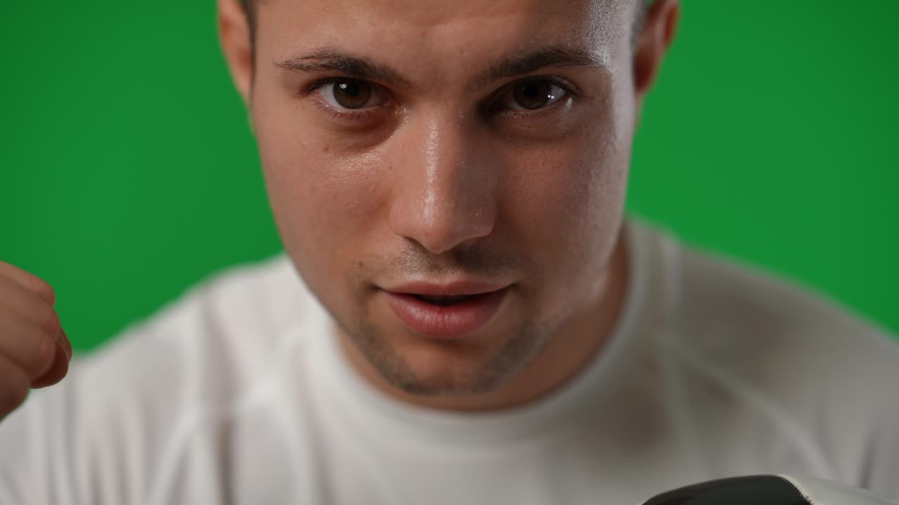 Close-up portrait of satisfied young sportsman with brown eyes looking at camera gesturing success. Front view headshot of confident skilled footballer posing at chromakey green screen background.