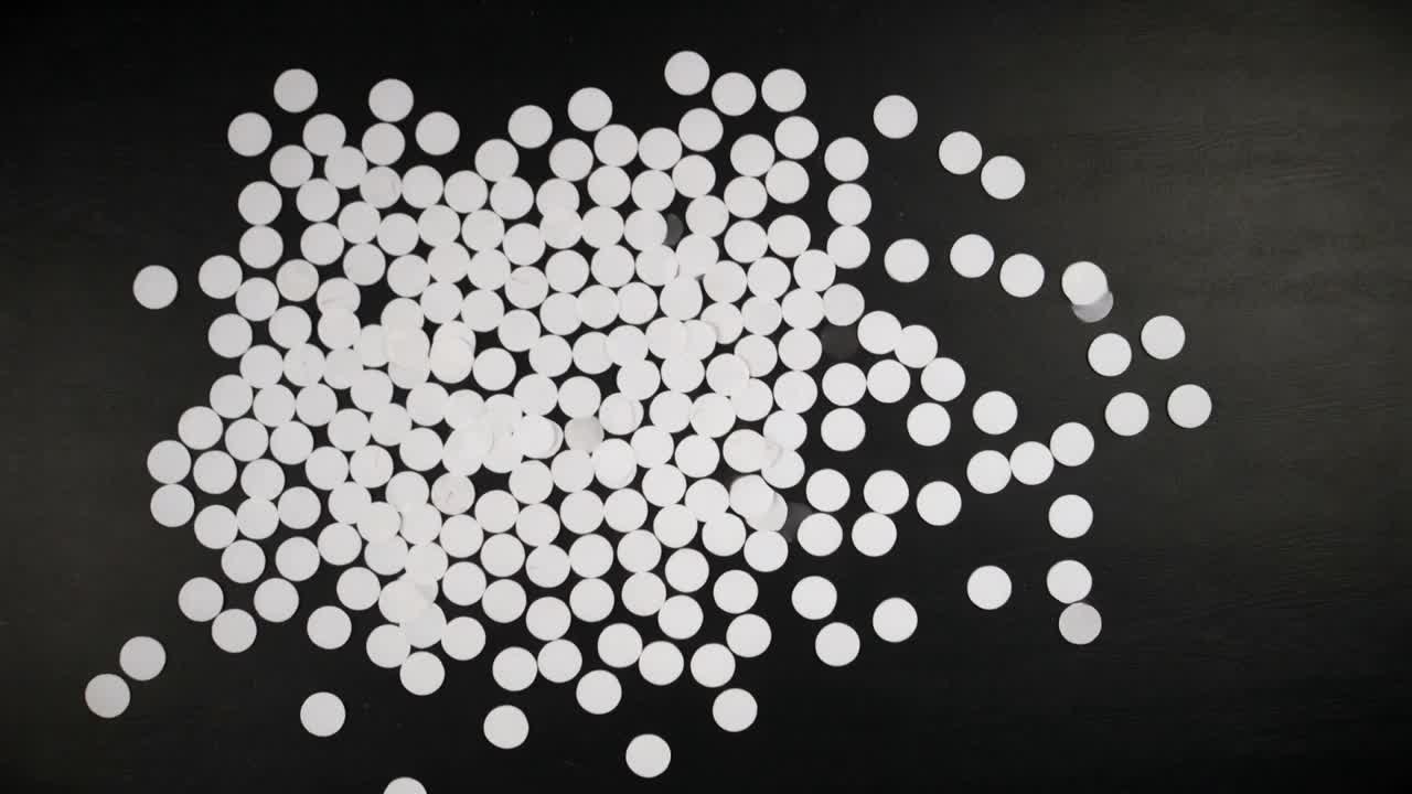 Sliding cluster of small white circular discs consolidating on black mat, forming central rectangle