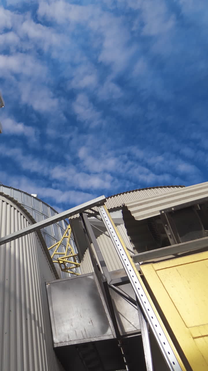 Metal construction of industrial plant. Industrial equipment of a modern agricultural complex for storing and processing grains against blue sky. Vertical video